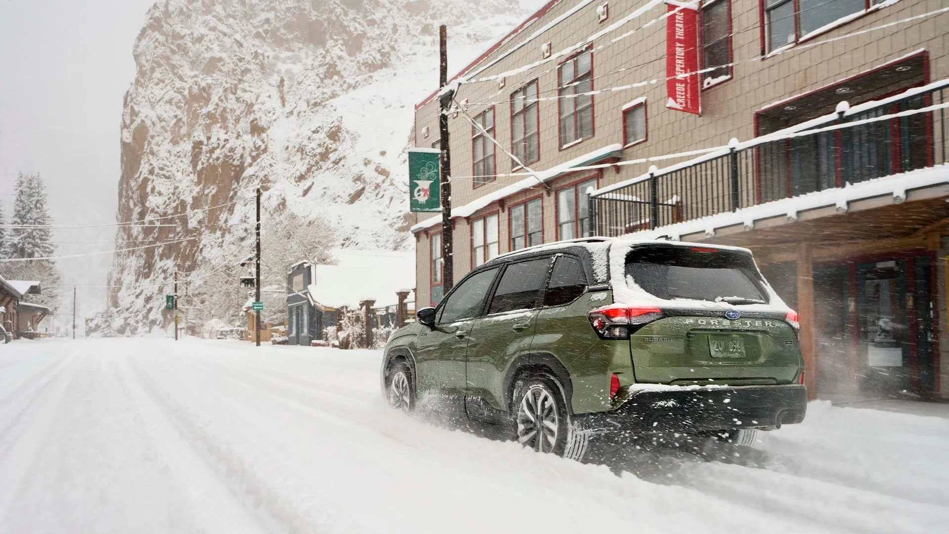 Subaru Forester Hybrid 2025 màu xanh lá đang chạy trên đường phủ tuyết ở thành phố, chụp góc 3/4 phía sau