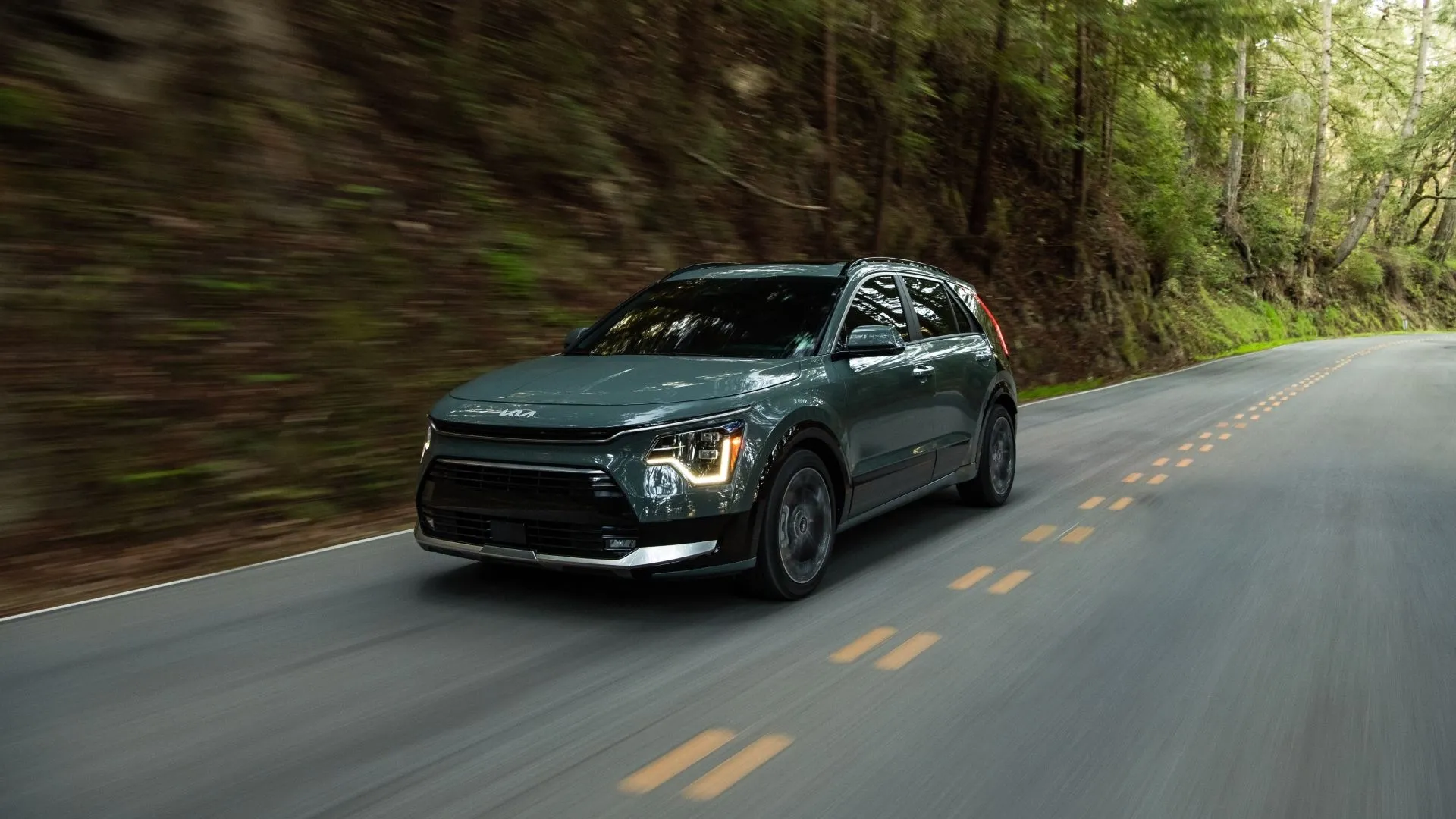 SUV Kia Niro Hybrid 2025 màu xanh ngọc, góc 3/4 phía trước đang di chuyển, sở hữu thiết kế hiện đại và tiết kiệm nhiên liệu.