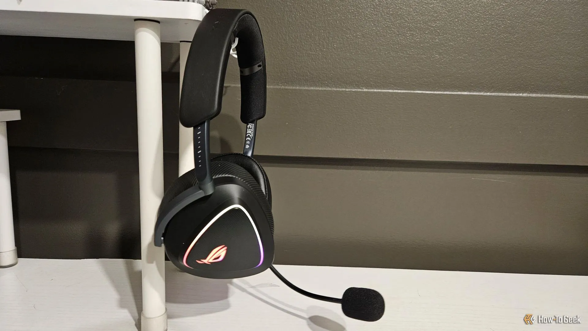 Tai nghe ASUS ROG Delta II màu đen treo gọn gàng trên giá đỡ bên cạnh màn hình máy tính.