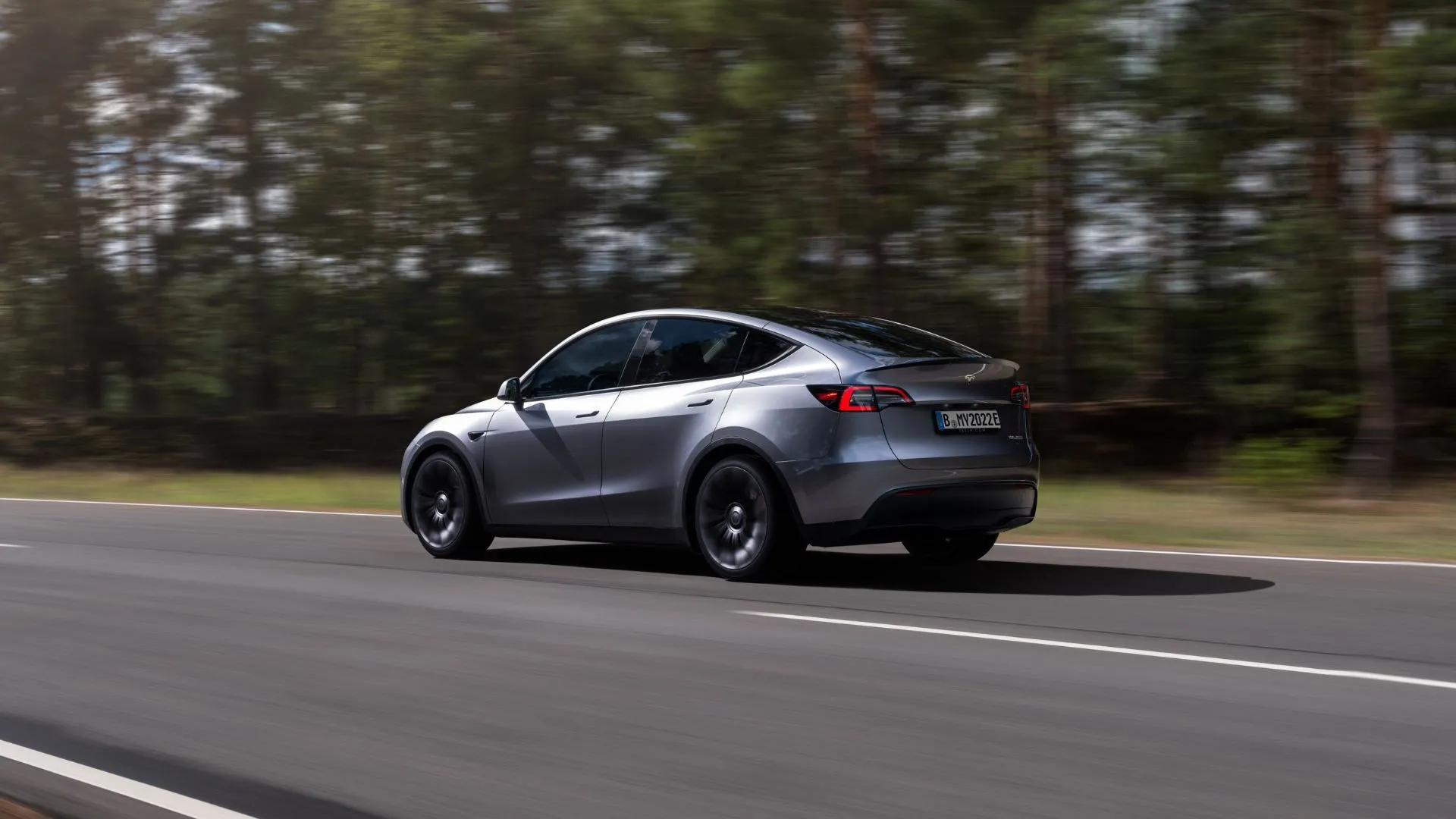 Tesla Model Y màu bạc di chuyển qua rừng, nhấn mạnh chính sách bảo hành và độ bền của pin xe điện.