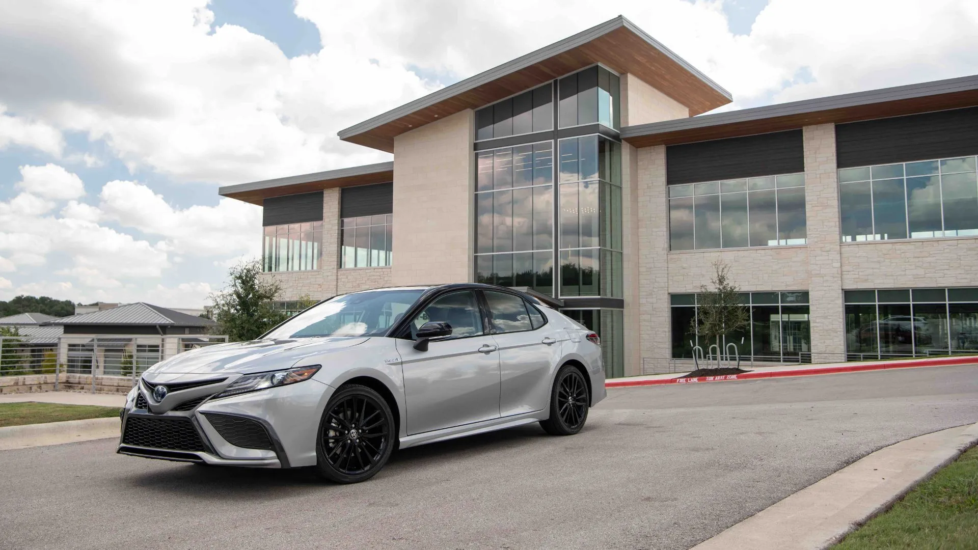 Toyota Camry Hybrid 2022 XSE màu bạc đỗ bên ngoài một tòa nhà hiện đại, nhấn mạnh sự hòa hợp giữa thiết kế xe và môi trường đô thị.