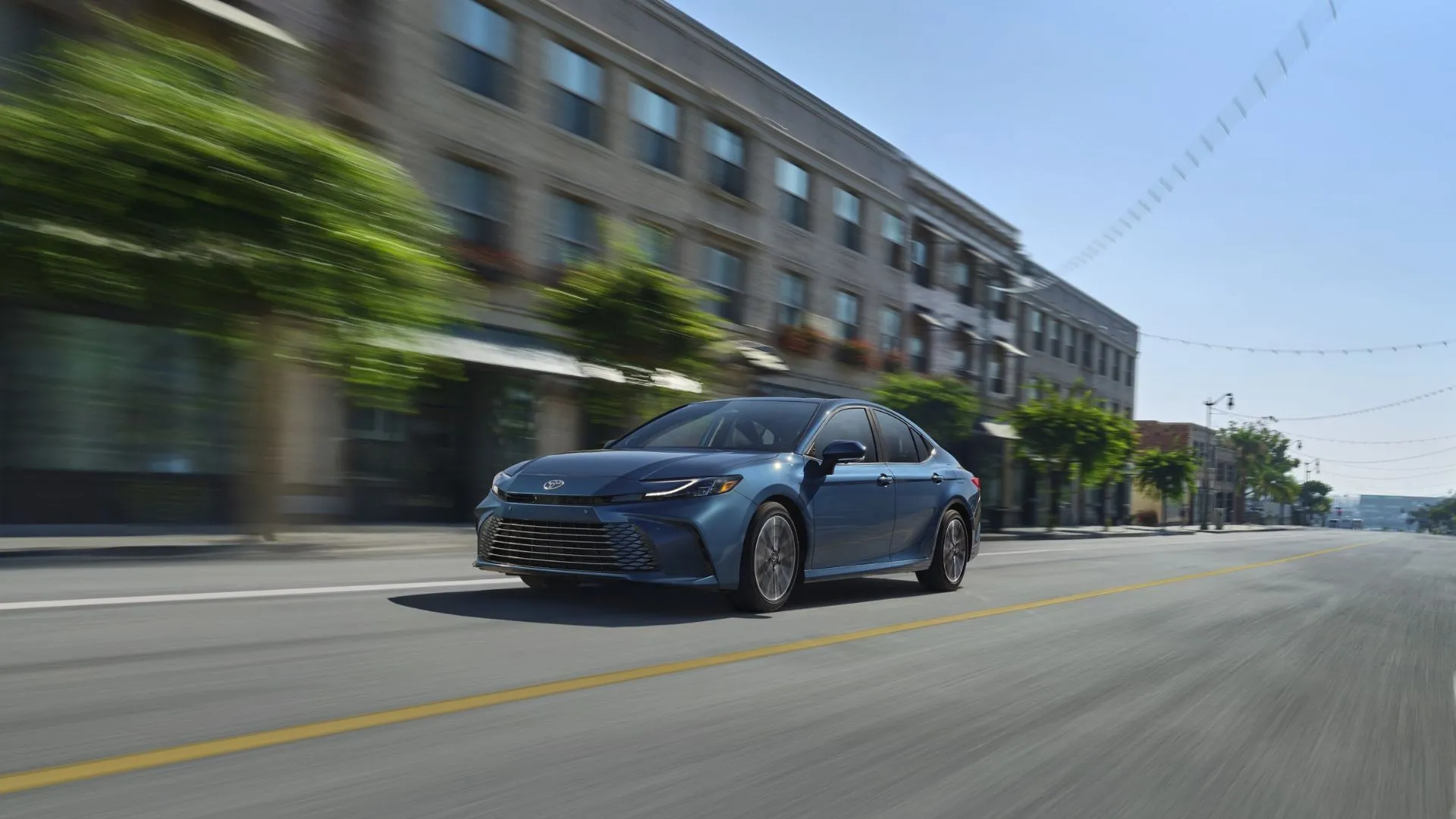 Toyota Camry Hybrid LE 2025 màu xanh lam lướt êm ái trên đường phố, kết hợp giữa sự sang trọng và hiệu quả nhiên liệu vượt trội.