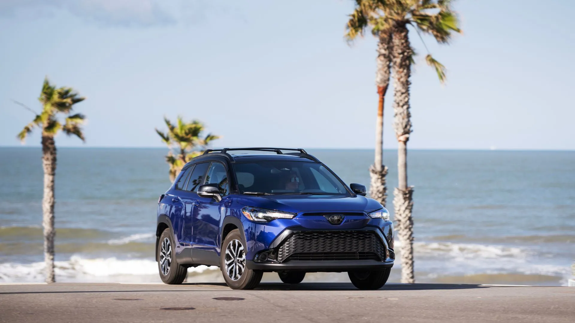 Toyota Corolla Cross Hybrid SE 2024 màu xanh Blue Crush Metallic đậu trước bãi biển, thể hiện thiết kế năng động và phù hợp với lối sống đô thị