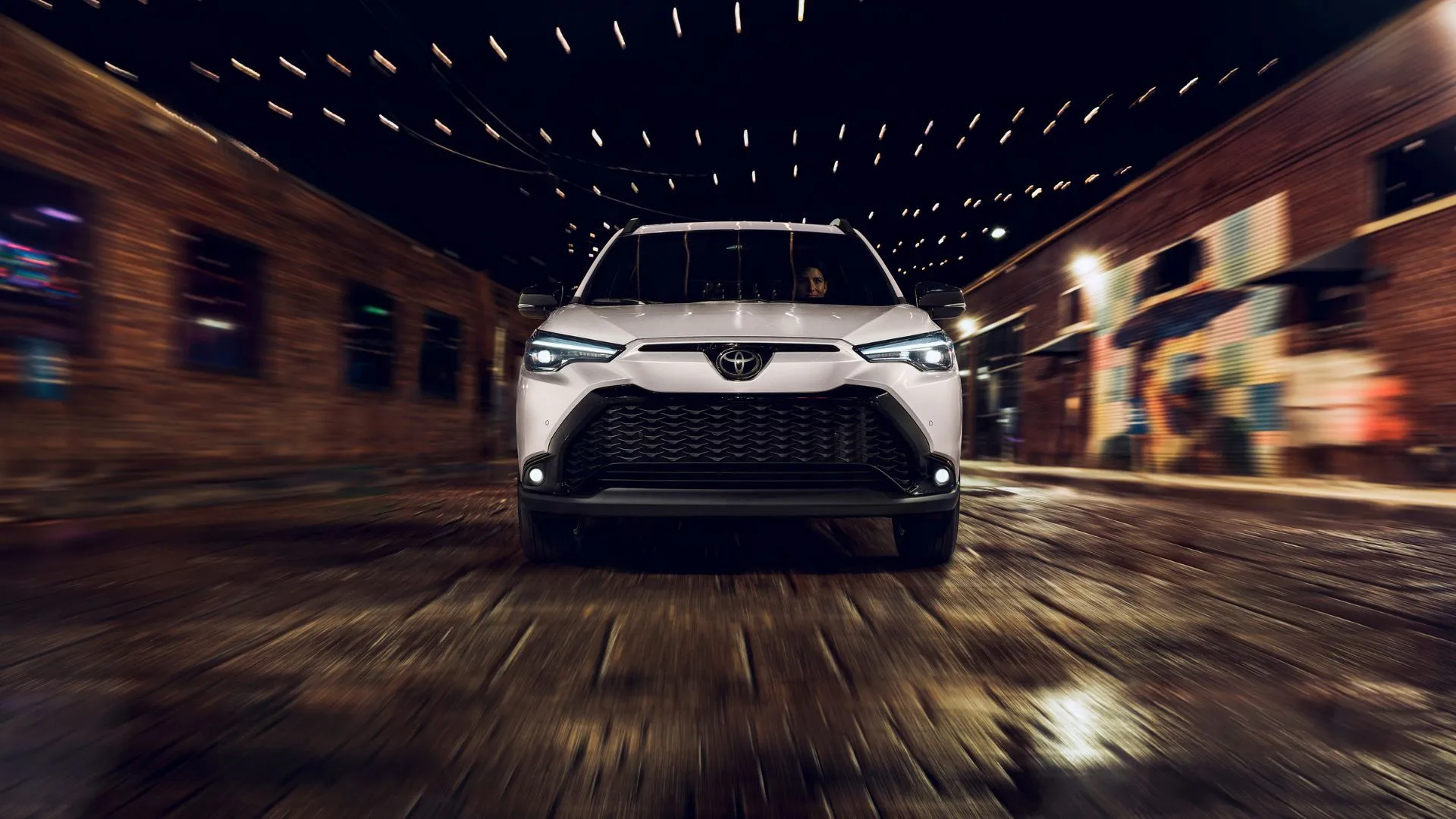 Toyota Corolla Cross Hybrid XSE 2025 màu trắng Wind Chill Pearl di chuyển trên đường phố lát đá cuội vào ban đêm, minh họa khả năng vận hành linh hoạt
