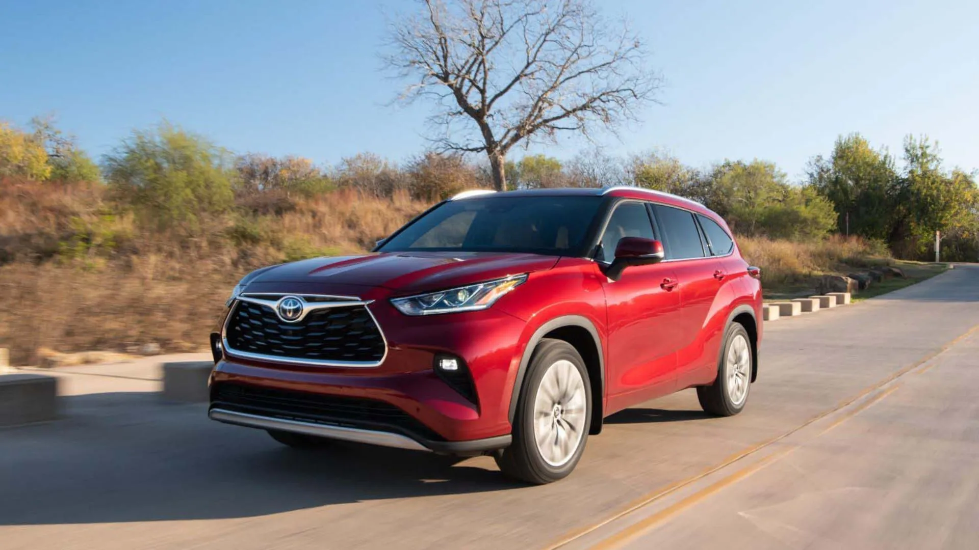 Toyota Highlander Platinum Hybrid 2025 màu đỏ, góc 3/4 phía trước, đang lái trên đường nông thôn