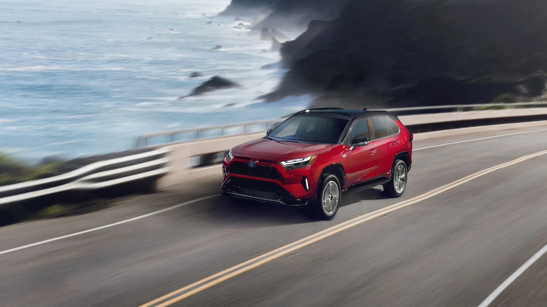 Toyota RAV4 Prime XSE 2024 màu đỏ di chuyển dọc con đường ven biển, nổi bật với thiết kế thể thao và hiệu suất cao của mẫu SUV hybrid plug-in.