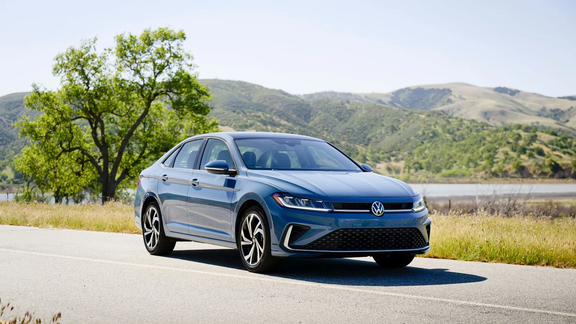 Volkswagen Jetta 2025 màu xanh lam đậu giữa cây xanh và đồi núi.