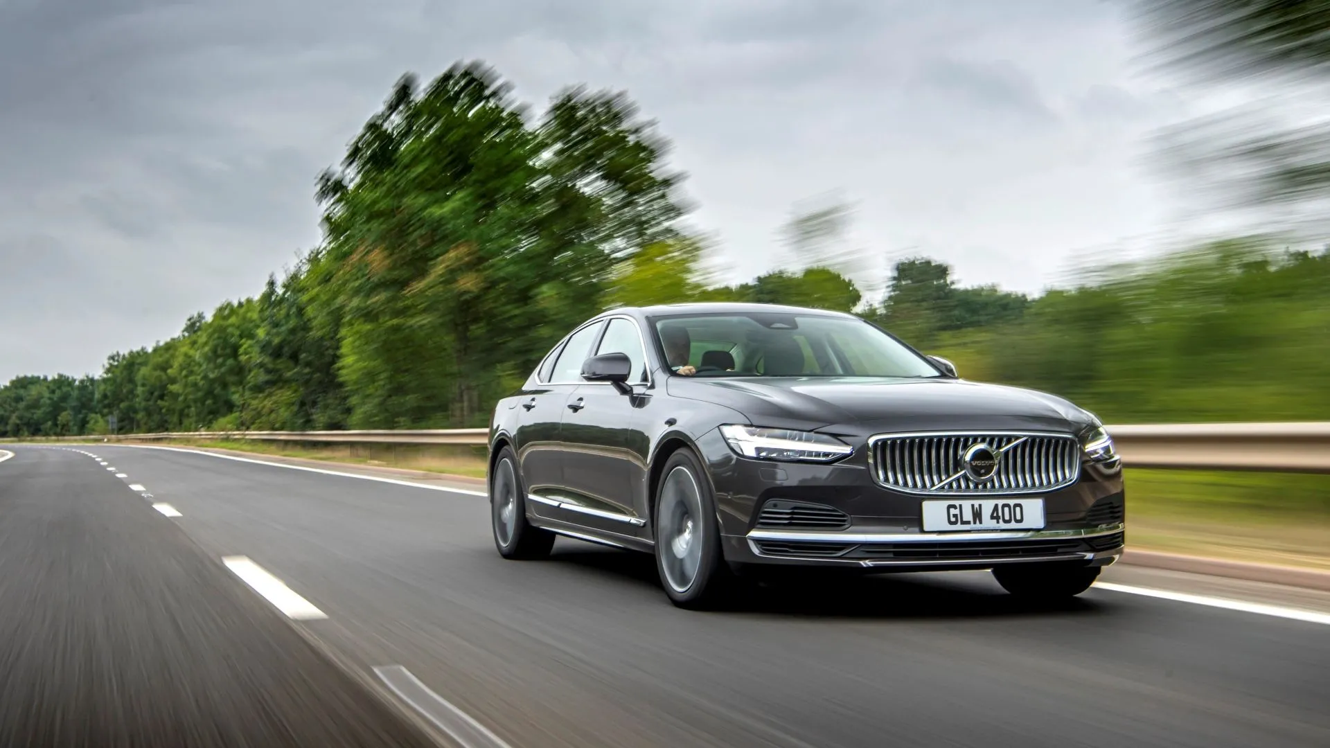 Volvo S90 2025 màu xám bạc đang di chuyển, với góc nhìn 3/4 phía trước, thể hiện sự sang trọng tinh tế và thiết kế hiện đại của mẫu sedan Thụy Điển.