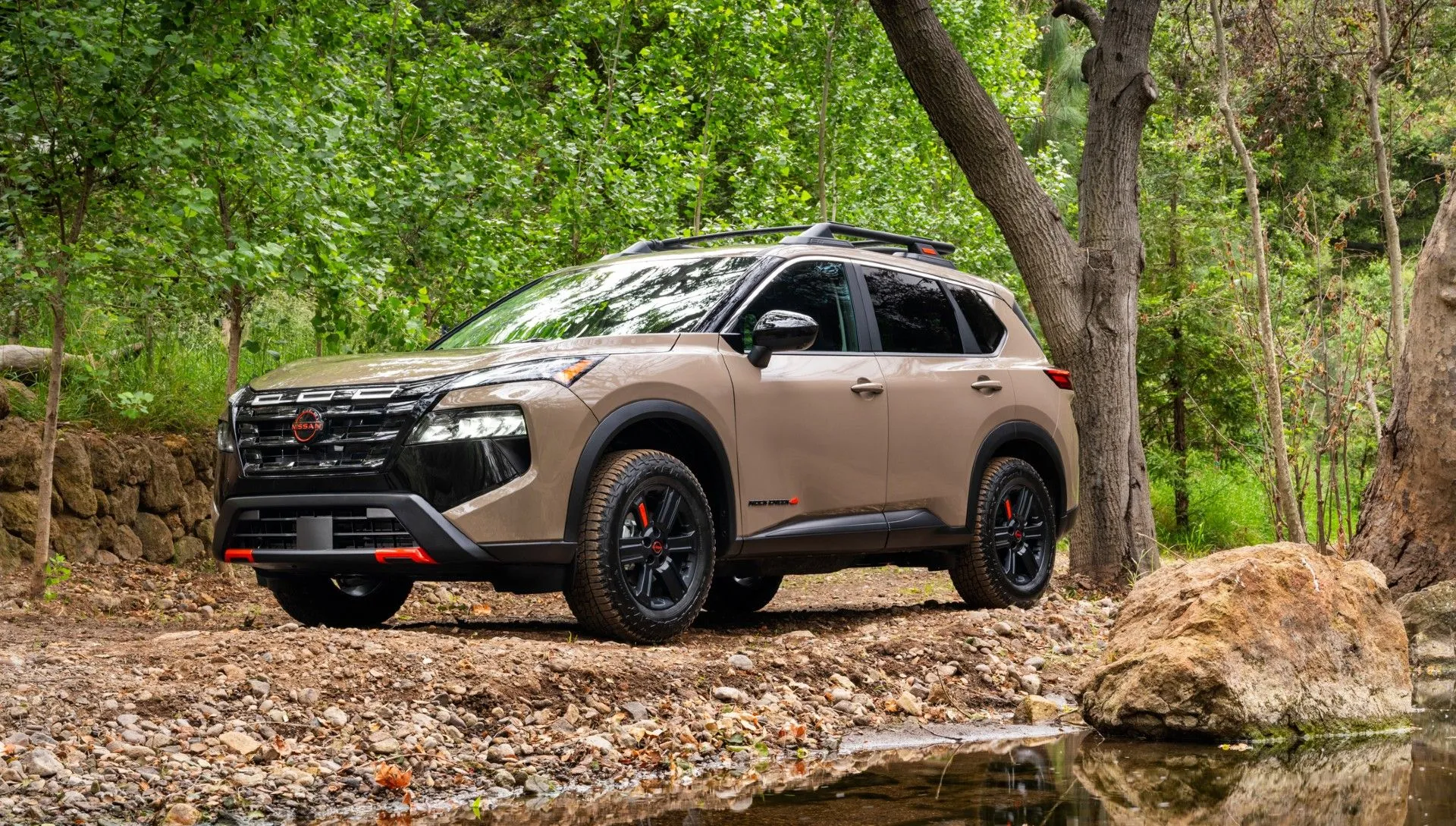 Xe Nissan Rogue 2024 màu xanh lam đỗ trong khu rừng, nổi bật với phong cách thiết kế mạnh mẽ và hiện đại.