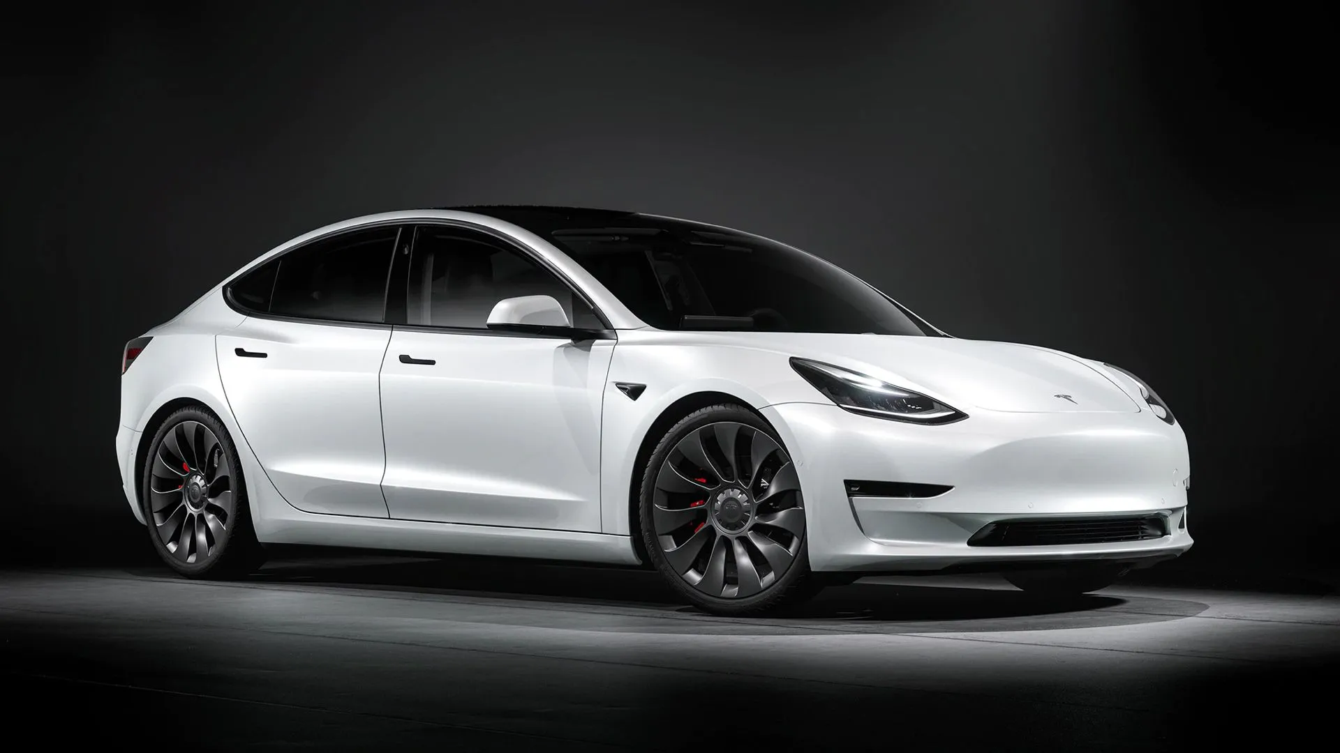 Xe Tesla Model 3 đời 2021 màu đen đang đỗ trước tòa nhà với cửa kính phản chiếu bầu trời, biểu tượng cho sức mạnh hệ truyền động và các linh kiện bền bỉ giúp xe đạt quãng đường di chuyển ấn tượng.