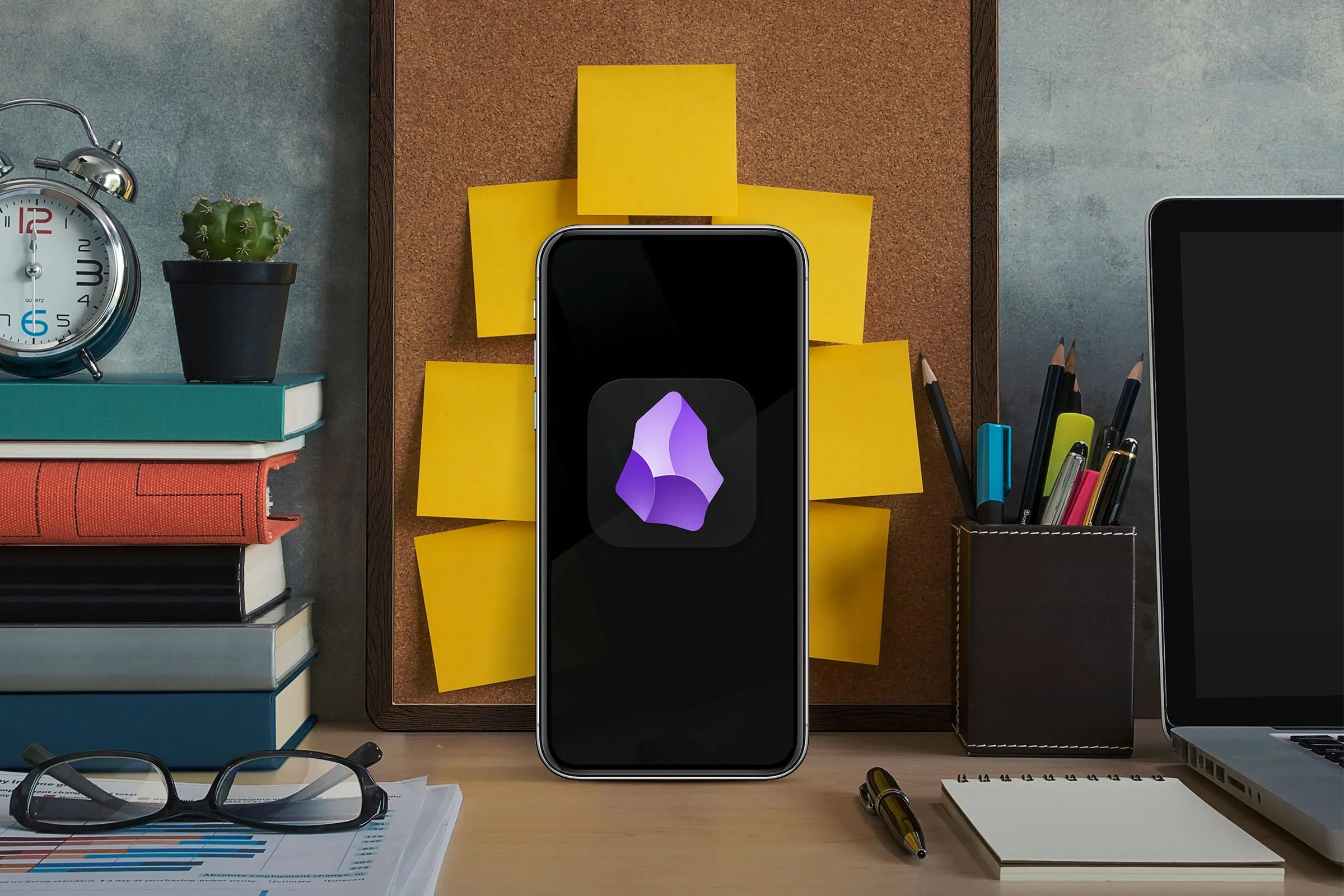 Một chiếc điện thoại thông minh trên bàn làm việc cùng sách và laptop, thể hiện sự hội tụ của công nghệ di động và máy tính