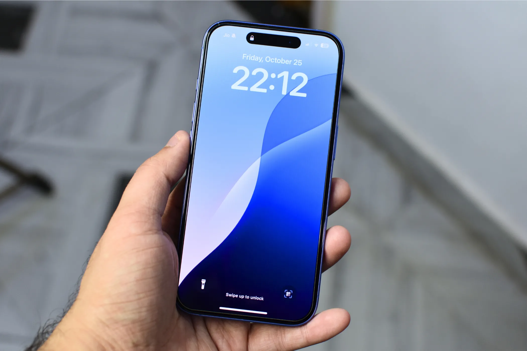 Người dùng cầm trên tay một chiếc iPhone 16, màn hình hiển thị hình nền khóa màu xanh, tượng trưng cho trải nghiệm sử dụng smartphone.